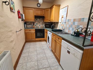 A kitchen with wooden cabinets countertops a washing machine dishwasher sink and appliances at Puffin Cottage in Llanboidy