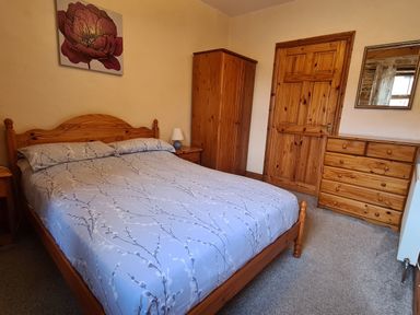 A bedroom with a wooden bed a matching wardrobe chest of drawers and a door with a framed flower picture on the wall at Puffin Cottage in Llanboidy