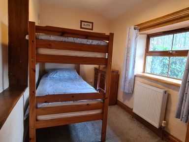 A bedroom with wooden bunk beds next to a window with floral curtains and a radiator at Puffin Cottage in Llanboidy