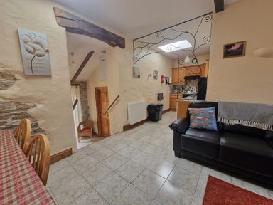 A tiled floor room with a black couch and kitchen area in the background at Puffin Cottage in Llanboidy
