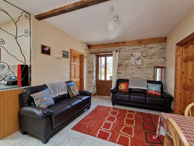 A living room with two black sofas with colorful cushions a red patterned rug and a wooden door at Puffin Cottage in Llanboidy