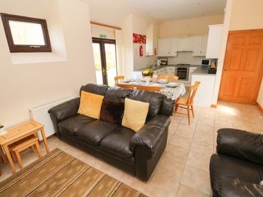 A living area with black sofas and a dining table set with chairs near a kitchen with white cabinets at Hill Top Farm Cottage Martletwy near Narbeth