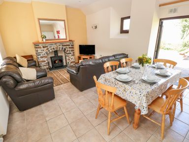 A living room with leather sofas a stone fireplace a television and a dining table set for six at Hill Top Farm Cottage in Martletwy near Narbeth
