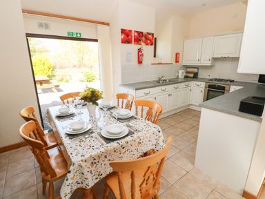 A kitchen with white cabinets a dining table set with plates glasses and cutlery and a fire exit door at Hill Top Farm Cottage Martletwy near Narbeth
