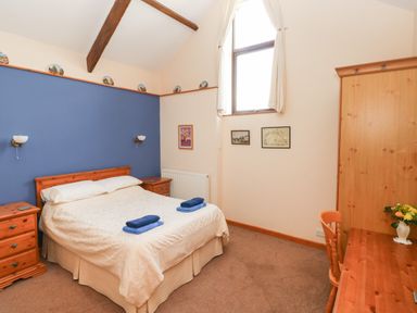 A bedroom with a double bed bedside tables a wooden wardrobe and a desk with a chair at Hill Top Farm Cottage Martletwy near Narbeth