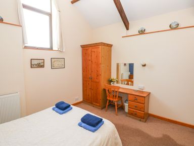 A bedroom with a bed with folded towels a wooden wardrobe a dressing table with mirror and chair at Hill Top Farm Cottage Martletwy near Narbeth