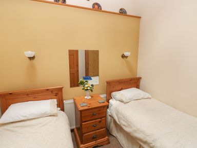 A bedroom with two single beds separated by a wooden nightstand with a flower vase at Hill Top Farm Cottage in Martletwy near Narbeth