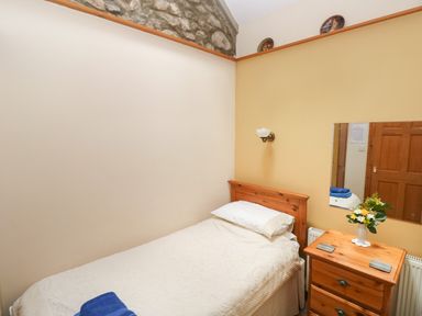 A small bedroom with a single bed wooden headboard a wooden bedside table with a vase of flowers and a mirror on the wall at Hill Top Farm Cottage Martletwy near Narbeth