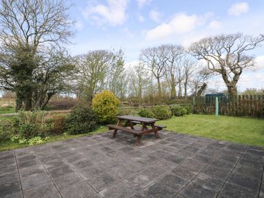 A patio with a wooden picnic table and a lawn with bushes and trees at Hill Top Farm Cottage Martletwy near Narbeth