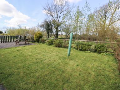 A garden with grass a covered rotary clothesline a wooden picnic table and trees at Hill Top Farm Cottage in Martletwy near Narbeth