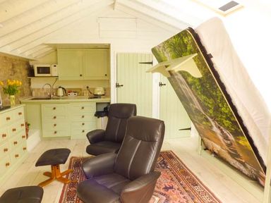 A small kitchen area with light green cabinets and black chairs with a fold-up bed in a white paneled room at Beech View in Malton