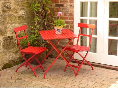 A red table with two red chairs and a potted plant on the table on a brick patio at Beech View in Malton