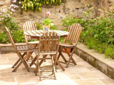 An outdoor patio area with a wooden round table and four wooden chairs with plants and flowers around at Beech View in Malton