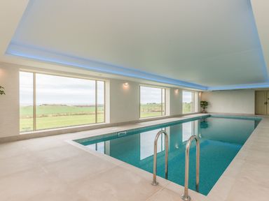 An indoor swimming pool with large windows overlooking green fields at Granary Stone House in Embleton