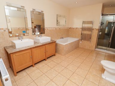 A bathroom with two sinks, a bath and a shower at Granary Stone House in Embleton