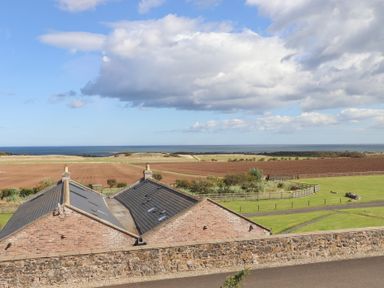 A view of houses and fields overlooking the ocean at Granary Stone House in Embleton