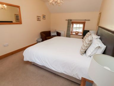 A bedroom with a bed and a chair at Granary Stone House in Embleton