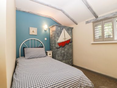 A bedroom with a single bed with checkered bedding a wooden wardrobe with a sailboat painting a nightstand and a window with shutters at Pear Tree Cottage in Mark near Burnham-on-Sea