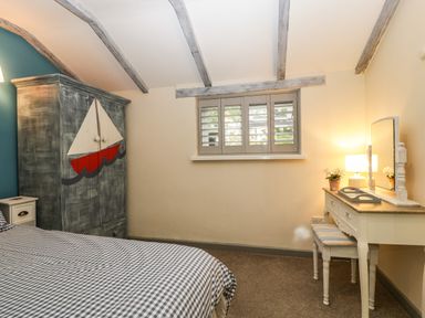A bedroom with a bed a wardrobe with a boat design a dressing table with a lamp and a window with shutters at Pear Tree Cottage Mark near Burnham-on-Sea