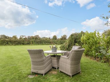A garden with a round table and four wicker chairs surrounded by plants and hedge at Pear Tree Cottage in Mark near Burnham-on-Sea
