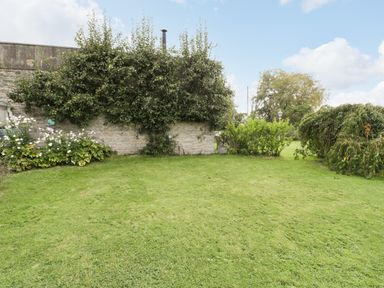 A garden with trimmed grass shrubs and a stone wall at Pear Tree Cottage in Mark near Burnham-on-Sea