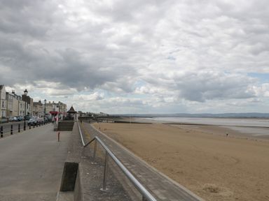 A beach with a promenade and buildings along the left side under a cloudy sky at Pear Tree Cottage in Mark near Burnham-on-Sea