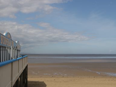A sandy beach with a pier and ocean under a partly cloudy sky at Burnham on Sea