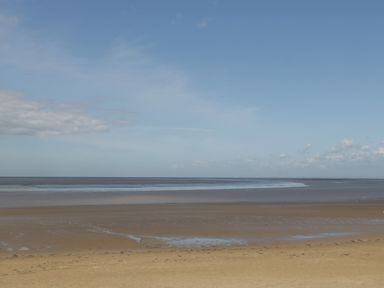 A sandy beach with shallow water and a blue sky with clouds at Pear Tree Cottage in Mark near Burnham-on-Sea