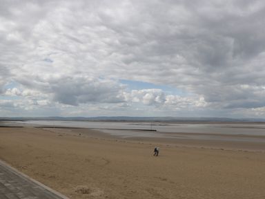 A sandy beach with two people walking and an expansive cloudy sky at Pear Tree Cottage in Mark near Burnham-on-Sea