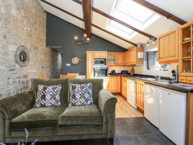 A kitchen with wooden cabinets and a sofa at Pear Tree Cottage Mark near Burnham-on-Sea