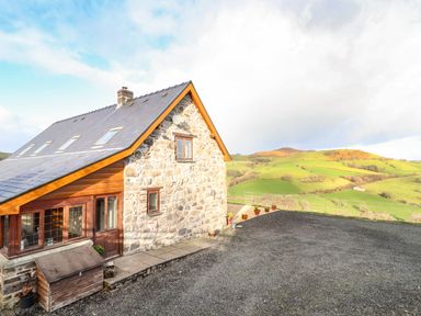 Stone and wood house with gravel driveway and green hills in the background at The Old House in Llanidloes