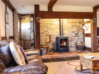 A living room with a leather sofa and pillows a stone fireplace with a wood stove and a wooden coffee table at The Old House in Llanidloes