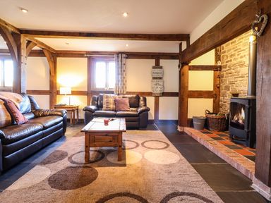 A living room with leather sofas a wooden coffee table a patterned rug and a wood burning stove at The Old House in Llanidloes