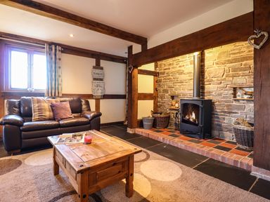 A living room with a leather sofa wooden coffee table rug and a fireplace with a wood stove at The Old House in Llanidloes