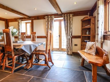 A dining room with wooden chairs and table near glass doors and a wooden bench with a cushion at The Old House in Llanidloes