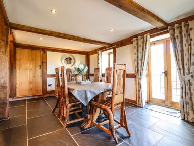 A dining room with wooden chairs and table near a wooden door and windows at The Old House in Llanidloes