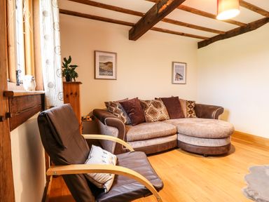 A living room with a brown sofa and a black armchair near a window at The Old House in Llanidloes