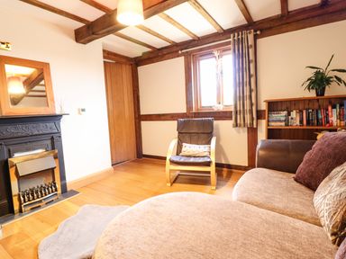 A living room with a fireplace an armchair a sofa a bookshelf and a wooden ceiling at The Old House in Llanidloes