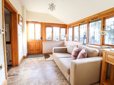A small sitting area with a beige sofa and cushions by windows and a wooden door at The Old House in Llanidloes