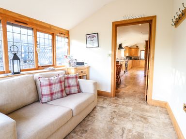 A sitting area with a beige sofa and plaid pillows next to windows and a doorway to a kitchen at The Old House in Llanidloes