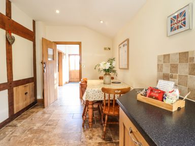 A dining area with a wooden table and chairs a countertop with a wooden tray of snacks and a tiled wall at The Old House in Llanidloes