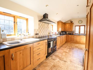 A kitchen with wooden cabinets black countertop a stove and windows at The Old House in Llanidloes