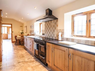 A kitchen with wooden cabinets a black stove and a dining table with chairs by a door at The Old House in Llanidloes