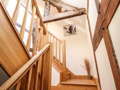 A wooden staircase with exposed beams a cow painting and dried plants at The Old House in Llanidloes