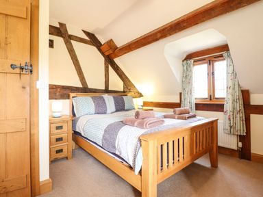 A bedroom with a wooden bed frame nightstand lamps and window with curtains at The Old House in Llanidloes