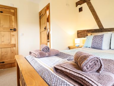 A bedroom with a bed made up with pillows and folded towels on top wood doors and a bedside table with a lamp at The Old House in Llanidloes