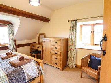 A bedroom with a bed folded towels wooden dresser desk wicker chair and floral curtains at The Old House in Llanidloes