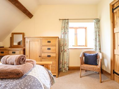 A bedroom with wooden furniture a wicker chair with a cushion and curtains on a window at The Old House in Llanidloes