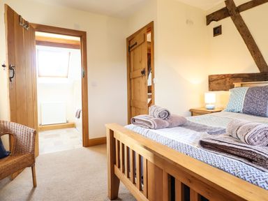 A bedroom with a wooden bed and towels on it next to a wicker chair and doors leading to a bathroom and another room at The Old House in Llanidloes