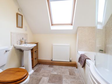 A bathroom with a toilet with wooden seat a pedestal sink a storage unit a bathtub with a towel and skylight window at The Old House in Llanidloes